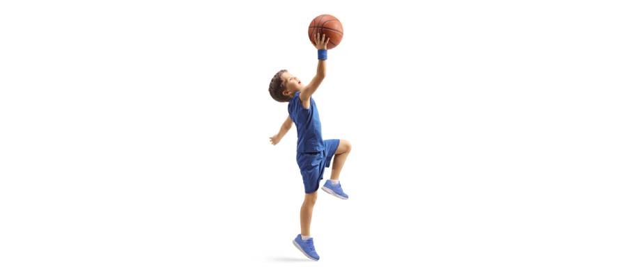 Mavi spor kıyafetli bir çocuk, tek ayak üzerinde sıçrayarak basketbol topunu potaya doğru uzatıyor. Beyaz arka planda, enerjik bir basketbol hareketi sergileniyor.