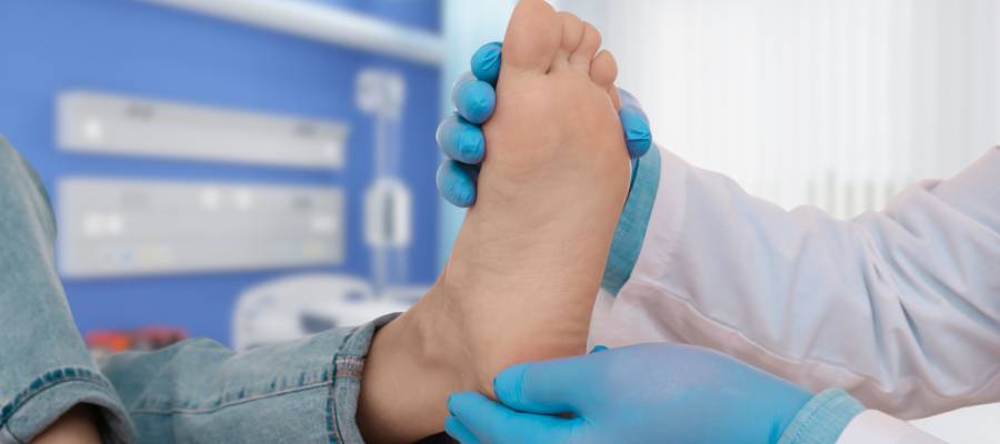 Doktor, mavi eldivenleriyle bir hastanın ayağını muayene ediyor.
